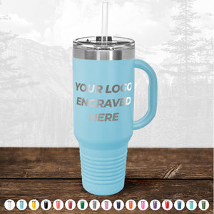 A light blue insulated tumbler with a straw and a text "custom logo engraved here" on it, displayed on a wooden surface with a faded forest background from TODAY ONLY - Custom Logo Drinkware Sale by Kodiak Coolers.