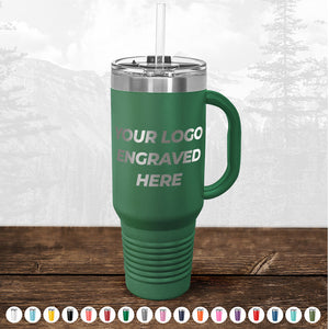 On a wooden surface with mountains behind, the Kodiak Coolers travel tumbler features a handle and straw. Engraved with "YOUR LOGO ENGRAVED HERE," this BLACK FRIDAY SALE custom mug is perfect for promotions. Multiple color options available—no setup fee!.