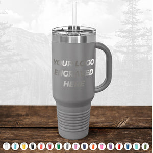 A Kodiak Coolers stainless steel travel mug with a handle and a lid, featuring a placeholder text "your custom logo here," set against a misty forest backdrop.