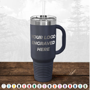 Navy blue insulated travel mug with handle and straw, featuring text "TODAY ONLY - Custom Logo Drinkware Sale - Your Logo Laser Engraved INCLUDED in Price - No Hidden Fee's" on a wooden table, with a misty forest background by Kodiak Coolers.