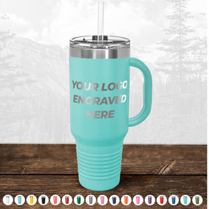 Kodiak Coolers aqua-colored insulated tumbler with a straw lid, custom printed with your logo, displayed on a wooden surface with a blurred forest background.