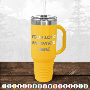 Yellow insulated travel mug with a handle and straw, featuring text "TODAY ONLY - Custom Logo Drinkware Sale - Your Logo Laser Engraved INCLUDED in Price - No Hidden Fee's" on it, displayed on a wooden surface against a blurry forest background by Kodiak Coolers.