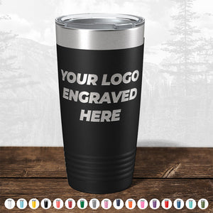 A black insulated travel mug with "your logo engraved here" text, perfect as a promotional gift, displayed against a blurred forest background from Kodiak Coolers.