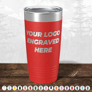 Red insulated tumbler from Kodiak Coolers with "your custom logo engraved here" text, displayed on a wooden surface against a blurred forest background.
