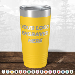 Yellow insulated Kodiak Coolers promotional gift tumbler with "your logo engraved here" text, displayed on a wooden surface against a blurred forest background.