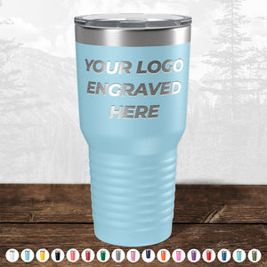 Promotional Kodiak Coolers blue stainless steel tumbler with custom logo engraving, displayed on a wooden surface against a forest backdrop.