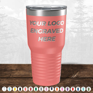 A pink insulated tumbler from Kodiak Coolers with "your logo engraved here" text, displayed on a wooden table against a forest background, perfect as a promotional gift.