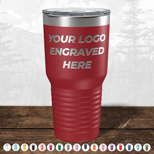 Red insulated tumbler with personalized engraving space on a wooden surface, blurred forest background. TODAY ONLY - Hump Day Sale - Your Logo Engraved on Kodiak Coolers Drinkware - Single Side Engraving Included in Price - Slider Lids Included