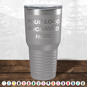 A TODAY ONLY - Custom Logo Drinkware Sale stainless steel insulated tumbler with text "your logo engraved here" on a wooden table against a forest background, ideal for a promotional gift by Kodiak Coolers.