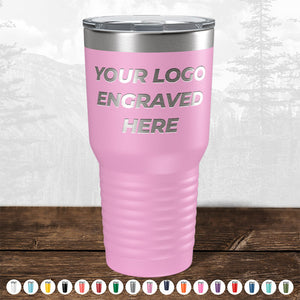 A pink insulated tumbler with a custom logo area on a wooden surface against a blurred forest background from Kodiak Coolers.