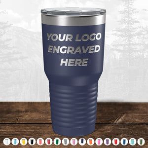 A TODAY ONLY - Custom Logo Drinkware Sale travel mug with "your logo engraved here" text, displayed on a wooden surface against a blurred forest background, perfect as a promotional gift by Kodiak Coolers.