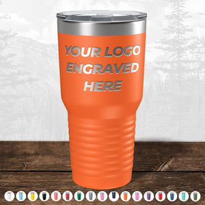 An orange insulated tumbler by Kodiak Coolers with a custom logo area, displayed on a wooden surface against a blurred forest background.