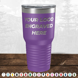 A purple insulated tumbler from Kodiak Coolers with "your custom logo engraved here" text, displayed against a blurred forest background.