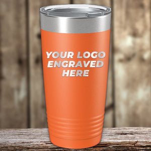 Orange insulated tumbler with a silver rim on a wooden surface, featuring the text "your logo engraved here" in white, available at wholesale pricing. Check out the Custom Tumblers 20 oz with your Logo or Design Engraved - Special Bulk Wholesale Pricing by Kodiak Coolers.