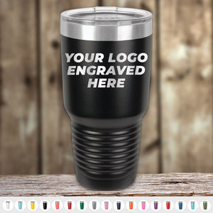 Kodiak Coolers Custom Tumblers with your logo or design engraved—no setup fees and $200 minimal order. Shown: black tumbler with clear lid on wood, displaying "YOUR LOGO ENGRAVED HERE." Color options are available below.