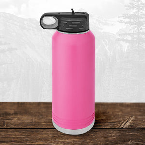 A 32 oz Wisconsin Green Bay Bulldogs water bottle by Kodiak Coolers, featuring a flip top straw lid and laser engraved design, sits on a wood surface with a faint mountain background.