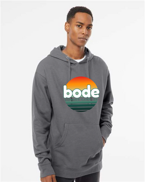 A person wears the Printify 2026 Bode Summer Bootcamp OG Logo Unisex Hoodie Sweatshirt (Independent Trading Co. SS4500) featuring a round sunset "bode" logo on the front, standing against a plain white background.