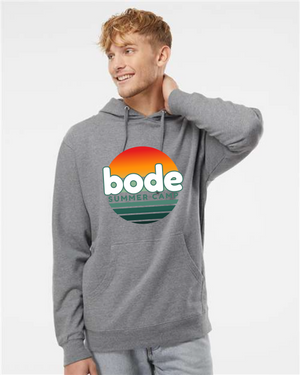 A person in a gray Printify 2026 Bode Summer Bootcamp — OG Logo Hoodie Sweatshirt (Unisex Independent Trading Co. SS4500) with a "bode summer camp" sunset graphic stands against a plain background.