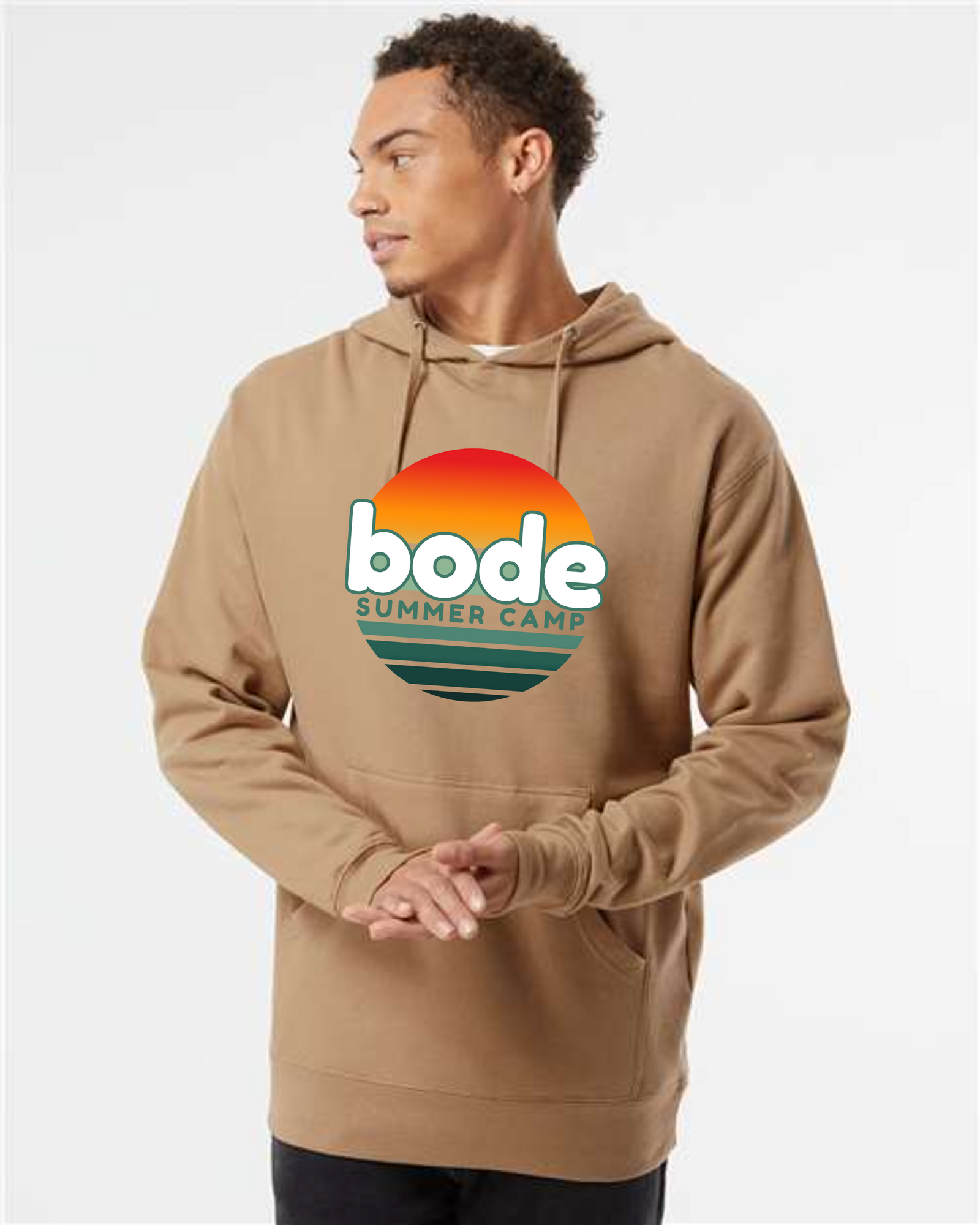 A person wears the Printify 2026 Bode Summer Bootcamp — Cali Sunset Hoodie Sweatshirt (SS4500), featuring a cotton-poly fleece and sunset logo, looking to the side against a plain background.