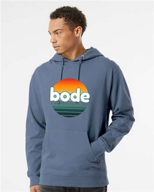 A man wears a Printify 2026 Bode Summer Bootcamp OG Logo Hoodie Sweatshirt (Unisex Independent Trading Co. SS4500) featuring a sunset graphic on the front.