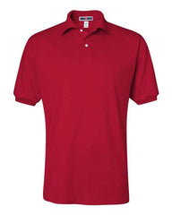 The JERZEES Midweight Polo Cotton Poly Blend SpotShield 50/50, a red short-sleeve shirt with a collar and two buttons near the neckline, featuring advanced SpotShield technology, is displayed on a plain white background.