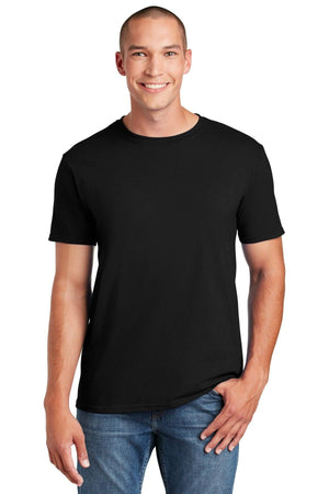 A person smiles in a black Gildan Softstyle T-Shirt 64000, made of ring spun cotton, and blue jeans, stands with one hand in their pocket against a white background. The modern classic fit by Gildan enhances their style while ensuring comfort.