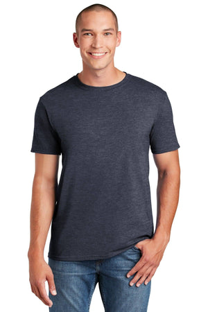 A person smiles against a white background, wearing the Gildan Softstyle T-Shirt 64000 in dark gray with a modern classic fit and jeans, one hand in their pocket.