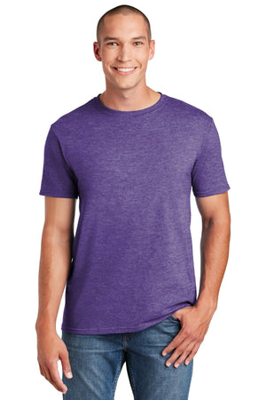 A person wearing a Gildan Softstyle T-Shirt 64000 in purple with a modern classic fit and blue jeans, standing and smiling against a white background.
