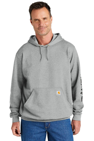 A man wearing a Carhartt Midweight Hoodie Logo Sweatshirt CTK288 and blue jeans stands against a plain white background, embodying the essence of durable workwear.