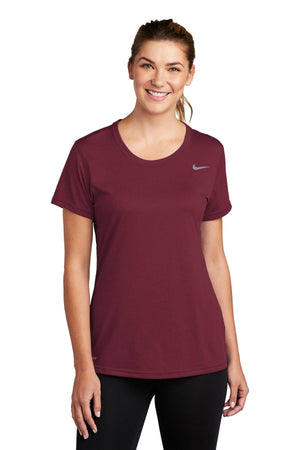 A woman wearing a maroon Nike Ladies Legend T-Shirt CU7599 and black leggings, both featuring Dri-FIT technology, standing with her hands on her hips and smiling at the camera.