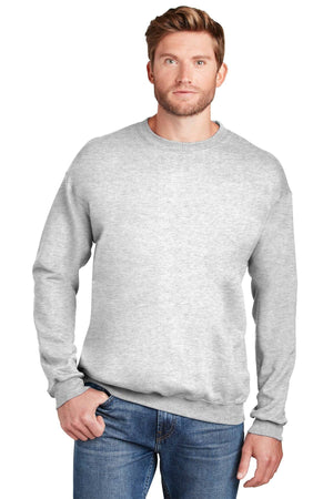 A man is wearing the Hanes Ultimate 100% Cotton Crewneck Sweatshirt F260 in light gray, paired with blue jeans, standing with one hand in his pocket against a white background.