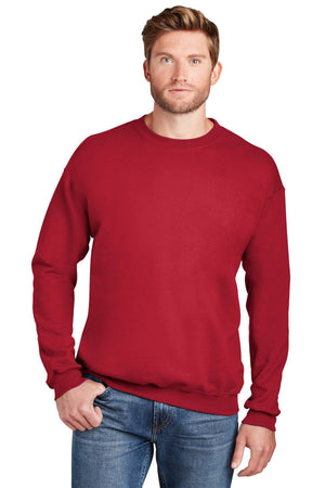 A man wearing the Hanes Ultimate 100% Cotton Crewneck Sweatshirt F260 in red and blue jeans stands with one hand in his pocket against a white background.