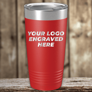 A red Kodiak Coolers stainless steel tumbler with your custom company logo engraved, ideal as a realtor closing gift for clients, shown on a wooden surface with a blurred wooden background.