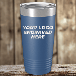 A blue Kodiak Coolers tumbler with a stainless steel lid sits on a wooden surface, featuring "YOUR LOGO ENGRAVED HERE"—ideal as Realtor closing gifts for clients or personalized company drinkware.