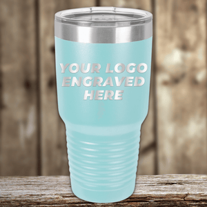 A light blue Kodiak Coolers tumbler with a clear lid rests on wood, engraved with "Your Custom Company Logo"—perfect as Realtor Closing Gifts for Clients or anyone seeking custom branded drinkware.