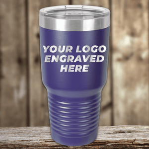 A blue Kodiak Coolers tumbler with a clear lid sits on a wooden surface, engraved with "YOUR COMPANY LOGO"—an ideal Realtor closing gift and stylish alternative to mugs. Custom drinkware for your clients, perfect for brand promotion.