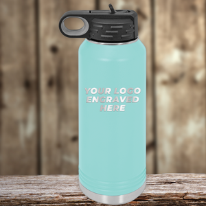 A light blue Kodiak Coolers bottle with a black lid rests on wood, featuring "YOUR LOGO ENGRAVED HERE." Ideal as a Realtor closing gift, it can display your custom company logo for clients.