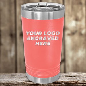 A coral-colored stainless steel tumbler by Kodiak Coolers with a clear lid sits on a wooden surface, engraved with "YOUR LOGO ENGRAVED HERE," making it an ideal Realtor closing gift or custom company logo drinkware for clients.