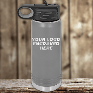 A gray Kodiak Coolers insulated water bottle with a black lid sits on a wooden surface, displaying “Your Custom Company Logo”—the ideal Realtor closing gift and perfect for promotional drinkware alongside custom logo mugs.