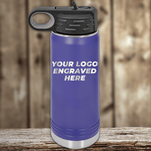 A blue Kodiak Coolers water bottle with a black lid sits on a wooden surface. Ideal as a realtor closing gift, it features "YOUR LOGO ENGRAVED HERE" showcasing your custom company logo on drinkware.