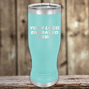 Customizable Kodiak Coolers teal Pilsner tumblers with space for engraved logo displayed on a wooden surface.