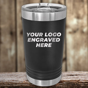 A black, stainless steel Kodiak Coolers Custom Pint Tumbler with customizable engraving on a wooden surface.