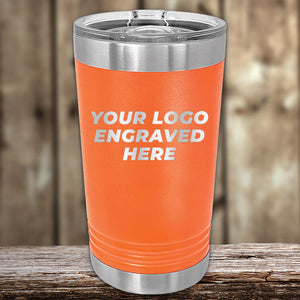 Orange Kodiak Coolers stainless steel pint glasses with customizable engraving space displayed on a wooden surface.