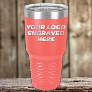 A coral-colored Kodiak Coolers custom tumbler engraved with the text "your logo here" displayed on its surface, set against a wooden background.
