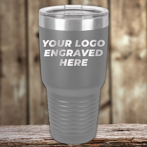 A Kodiak Coolers stainless steel tumbler with a customizable engraving area that reads "your logo engraved here," ideal as a corporate promotional gift, displayed on a wooden surface.