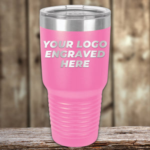 A pink Kodiak Coolers Engraved Custom Logo Drinkware tumbler with a clear lid sits on a wooden surface, showcasing how you can personalize mugs for your brand with single side engraving included in the price.