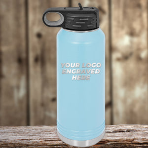 A light blue Kodiak Coolers stainless steel bottle with a black lid sits on a wooden surface. Part of the New Years Sale, it’s laser engraved with “YOUR LOGO ENGRAVED HERE”—customizable, no setup fee, and one side logo included.