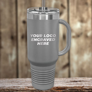 Gray insulated Kodiak Coolers travel mug with handle and straw, laser engraved with your custom logo—no setup fee, 1-side engraving included. Great personalized or promotional gift. Shown on a wooden surface with a blurred wood background. New Years Sale!.